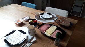 Una mesa de madera con un almuerzo que incluye jamón en rodajas, queso, pan, aderezos y una taza de café.