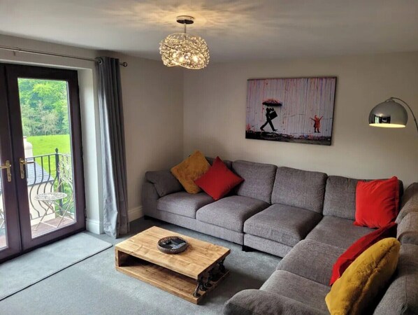 Un salon avec un canapé gris, une table basse en bois, un lustre et un tableau accroché au mur.