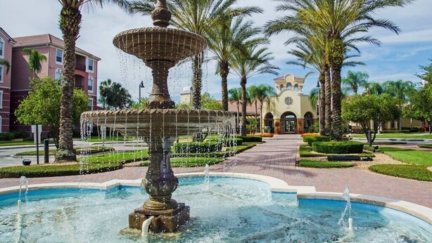 A fountain with multiple tiers and water jets, surrounded by palm trees and a building with arched windows in the background. - Spacious and Modern Townhome! Close to Attractions and Conventions Center! 3vc5014-10 (Orlando)