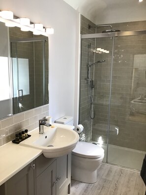 Un baño moderno con ducha envuelta en vidrio, un lavabo blanco y un espejo grande.