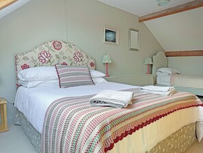 Un dormitorio con cama, almohadas, mesita de noche, lámparas y un cuadro en la pared.