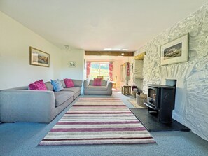 A cozy living room with a sofa, armchair, fireplace, and a view to the outside.