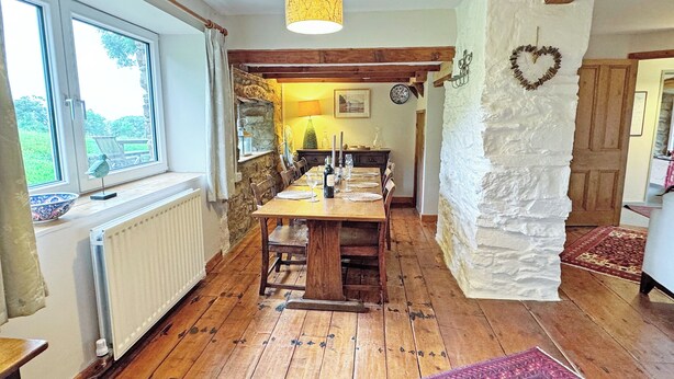 Un coin repas avec une table en bois, des chaises, un luminaire suspendu et un mur en pierre.
