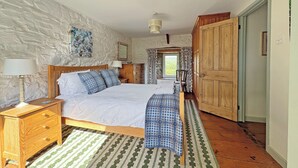 Une chambre à coucher avec un lit, des tables de chevet en bois, une commode, un tapis à motifs et un mur en pierre.