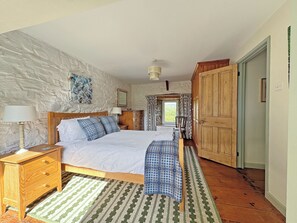 A bedroom with a bed, wooden nightstands, a dresser, a patterned rug, and a stone wall.