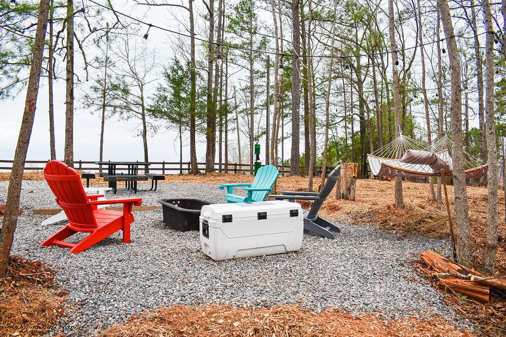 A campsite with outdoor seating, including red and blue Adirondack chairs, a white cooler, and a hammock.