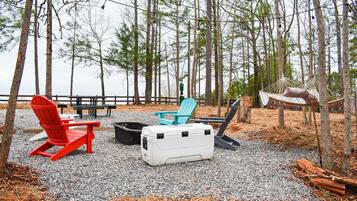 A campsite with outdoor seating, including red and blue Adirondack chairs, a white cooler, and a hammock.