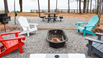 A gravel patio with Adirondack chairs, a fire pit, and a table with benches.