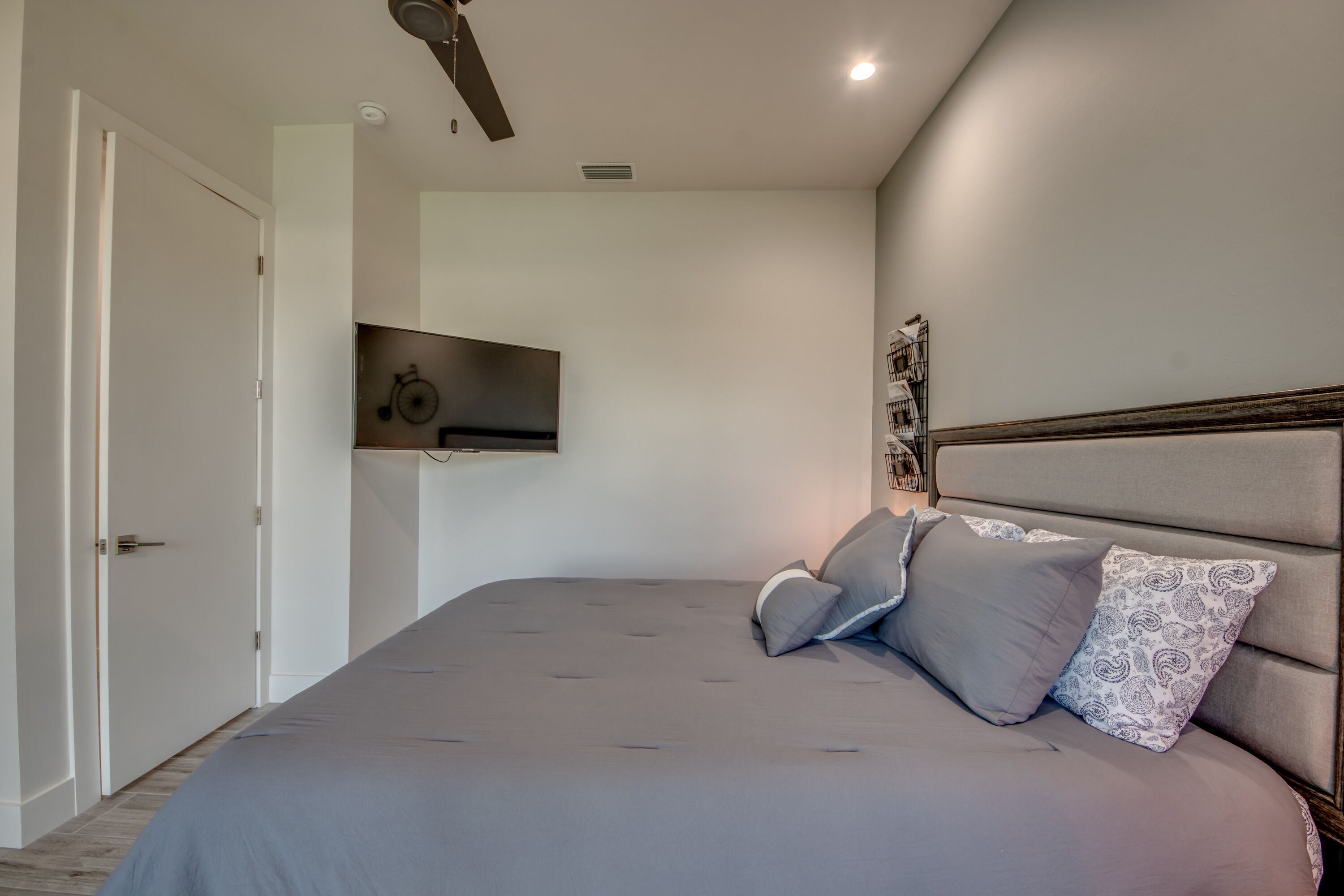 Une chambre moderne avec un grand lit, un ventilateur de plafond et un téléviseur fixé au mur.