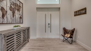 A modern interior with a wooden world map, a 'Welcome' sign, a cushioned chair, and a light-colored floor. - Heated pool & spa | New | Canal | Bikes | BBQ (Cape Coral)