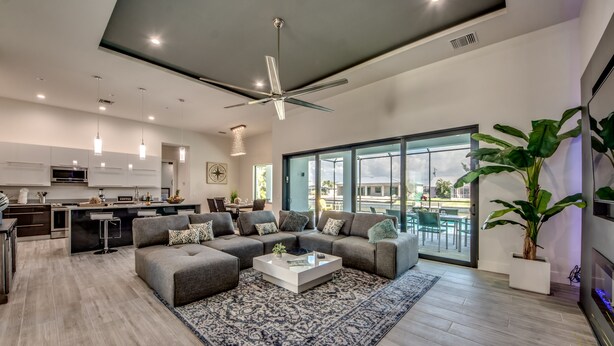 A modern living room with a sectional sofa, a coffee table, and a large window offering a view of the outdoors. - Heated pool & spa | New | Canal | Bikes | BBQ (Cape Coral)