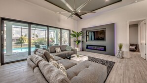 A modern living room with a large sectional sofa, a flat-screen TV mounted on the wall, and a ceiling fan. - Heated pool & spa | New | Canal | Bikes | BBQ (Cape Coral)