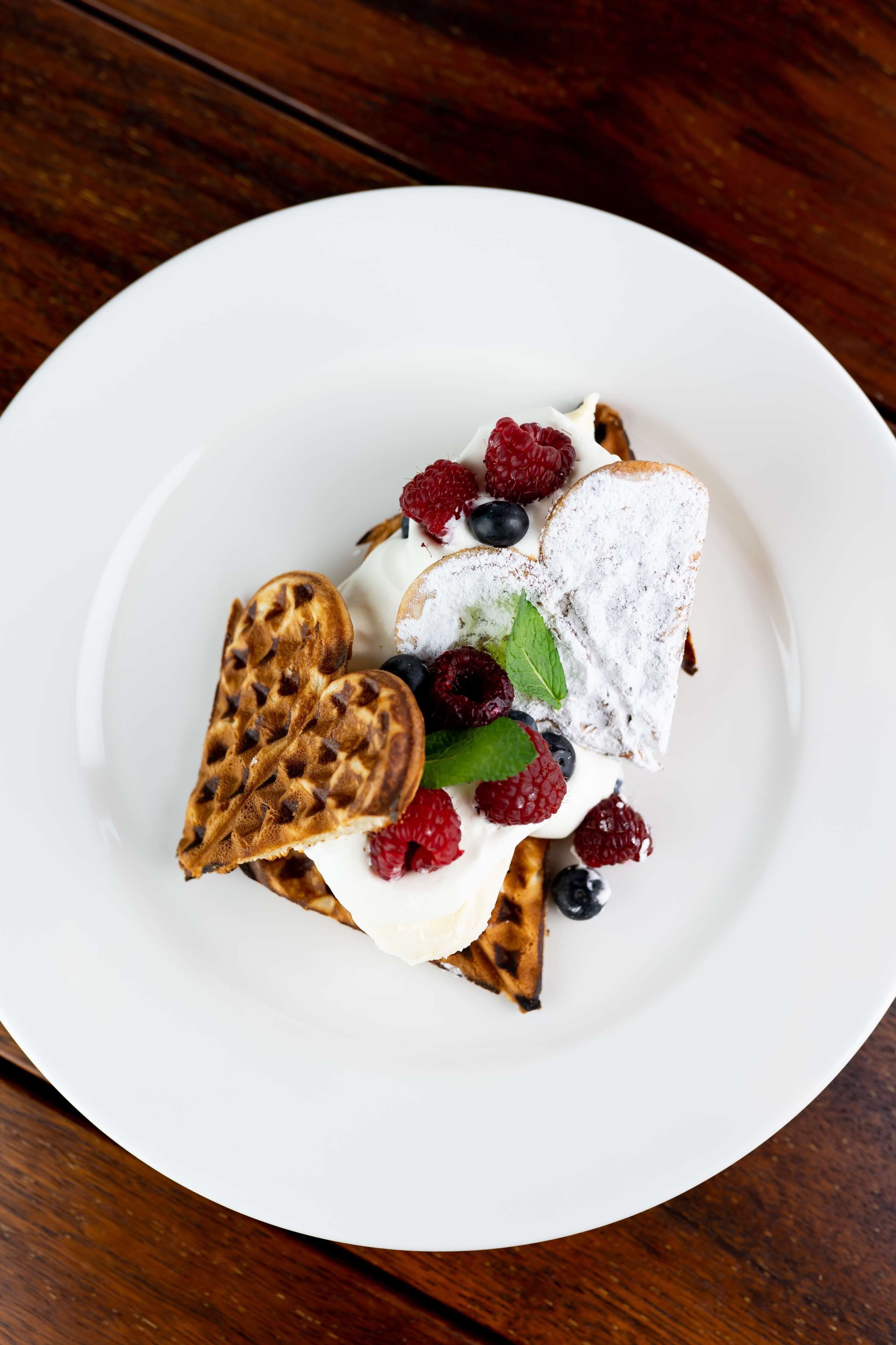 A plate with waffles, whipped cream, raspberries, blueberries, and a mint leaf.