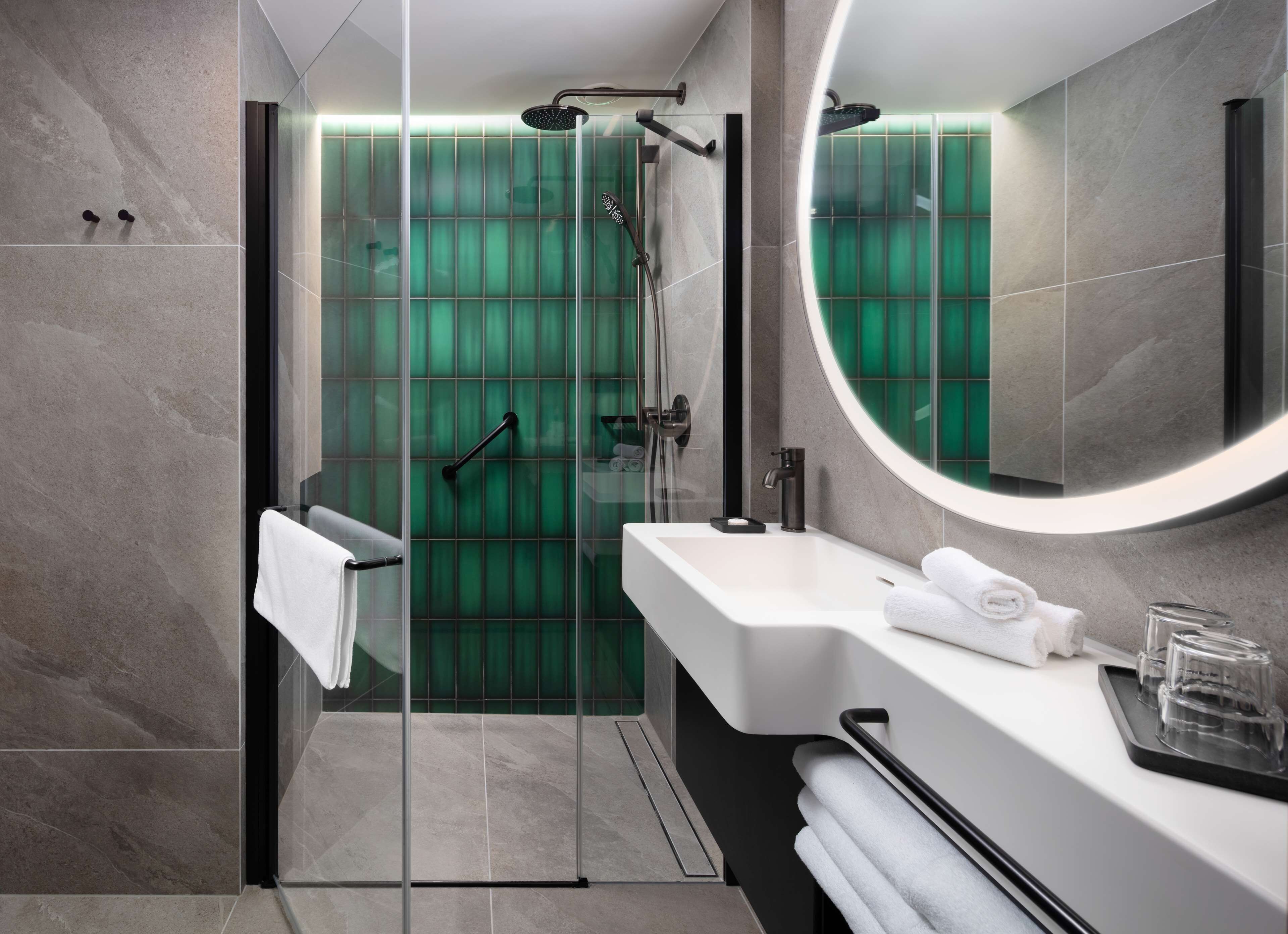 Un baño moderno con ducha envuelta en vidrio, un lavamanos blanco y un espejo grande.