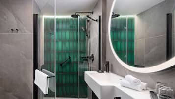 Un baño moderno con ducha envuelta en vidrio, un lavamanos blanco y un espejo grande.