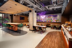 A modern restaurant with a wooden bar area, multiple seating arrangements, and a colorful mural on the wall. - Hyatt Place Krakow (Kraków)