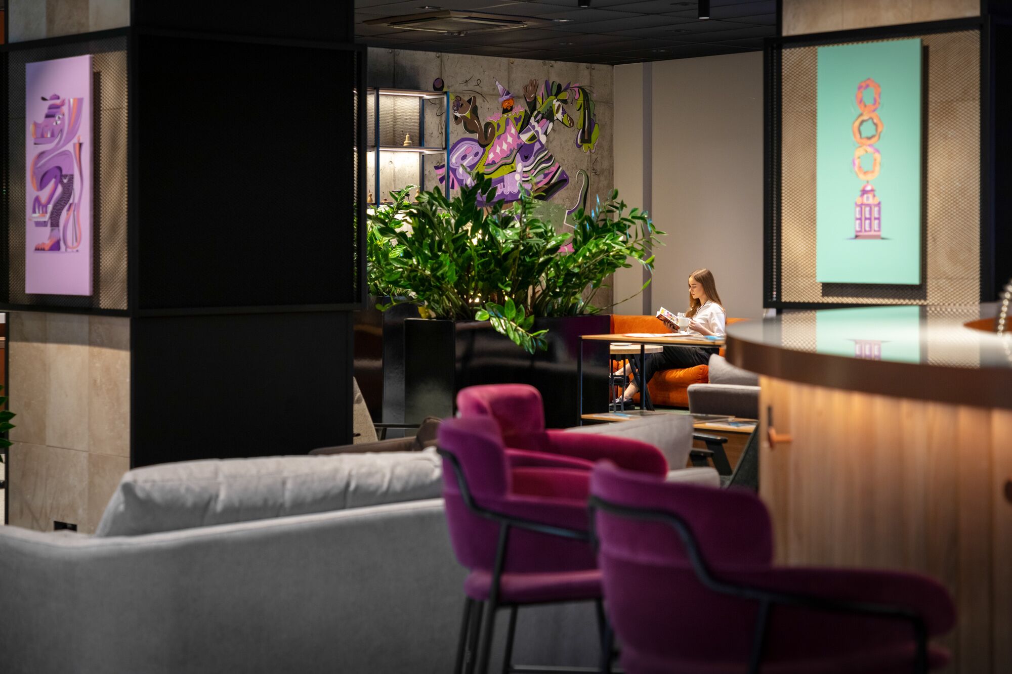 A modern lounge area with a seating arrangement, a large plant, and artwork on the walls.