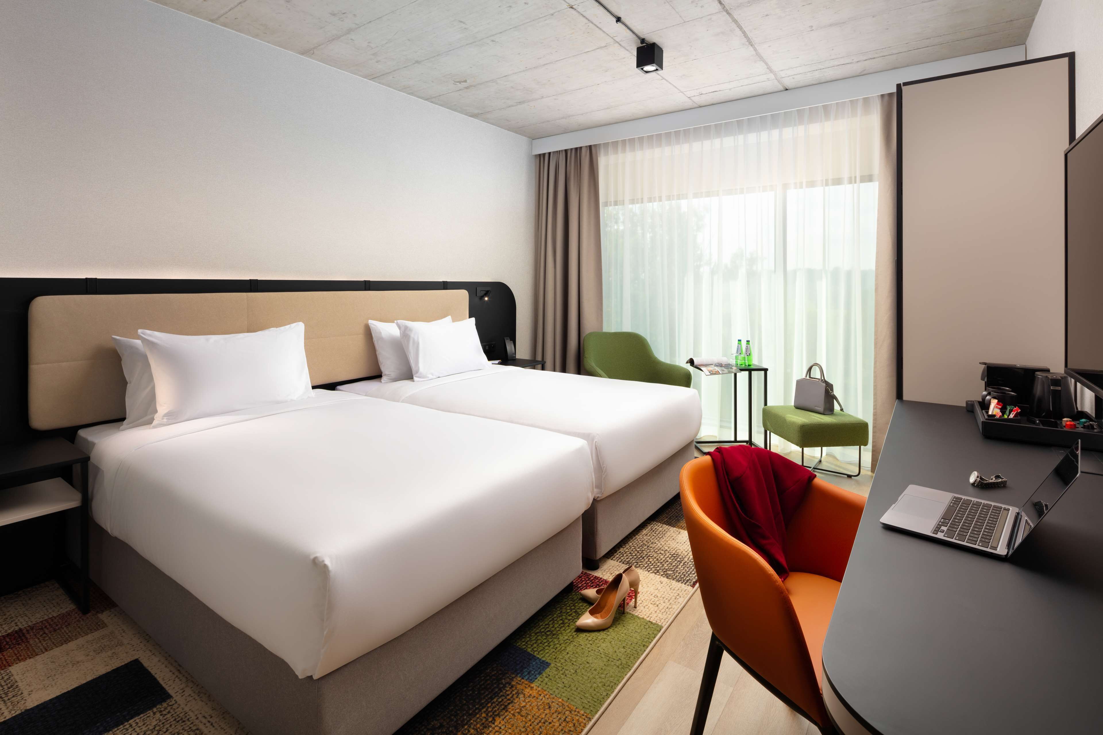 Habitació d'hotel amb dos llits, una taula de treball amb un portàtil, una cadira i una taula petita amb ampolles.