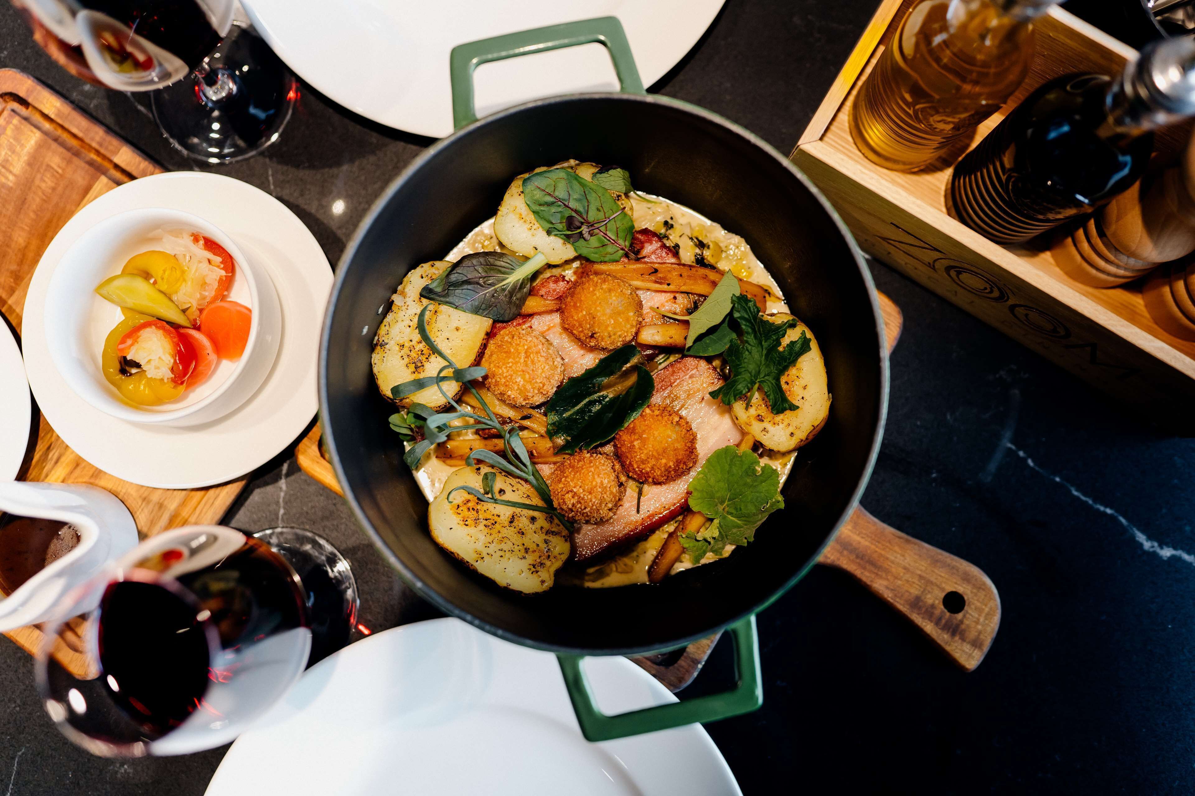 A pan with food, a bowl of vegetables, and wine glasses on a table.
