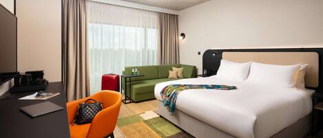 A hotel room with a bed, a desk, a green sofa, and a colorful rug.