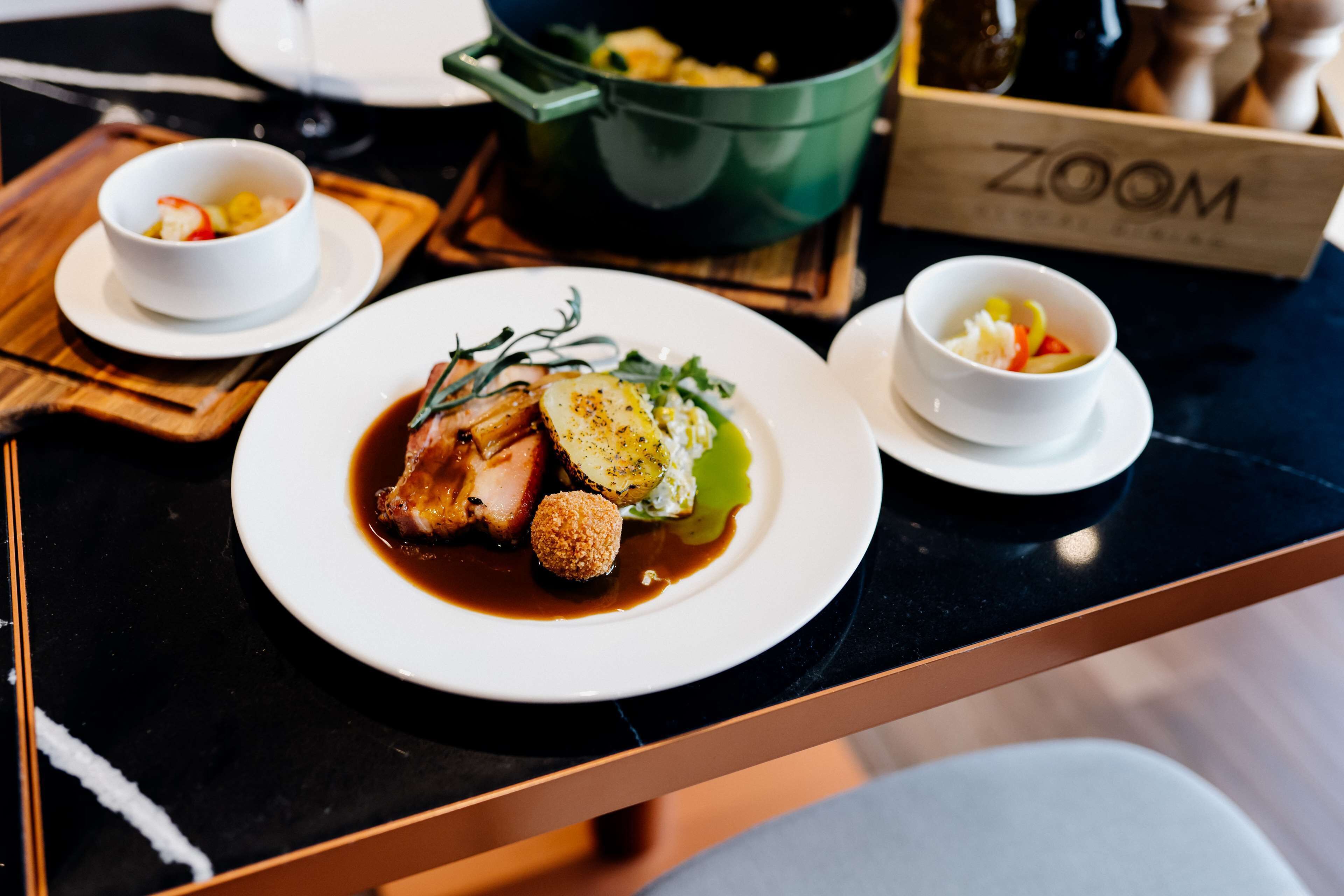 A dining table with plates of food, a green pot, and a box labeled "ZOOM".