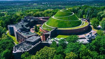 Vista aérea de un edificio histórico con un gran montículo central, rodeado de exuberante vegetación y un paisaje montañoso.