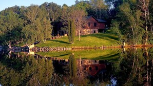 Une maison avec un étang devant, entourée d’arbres.