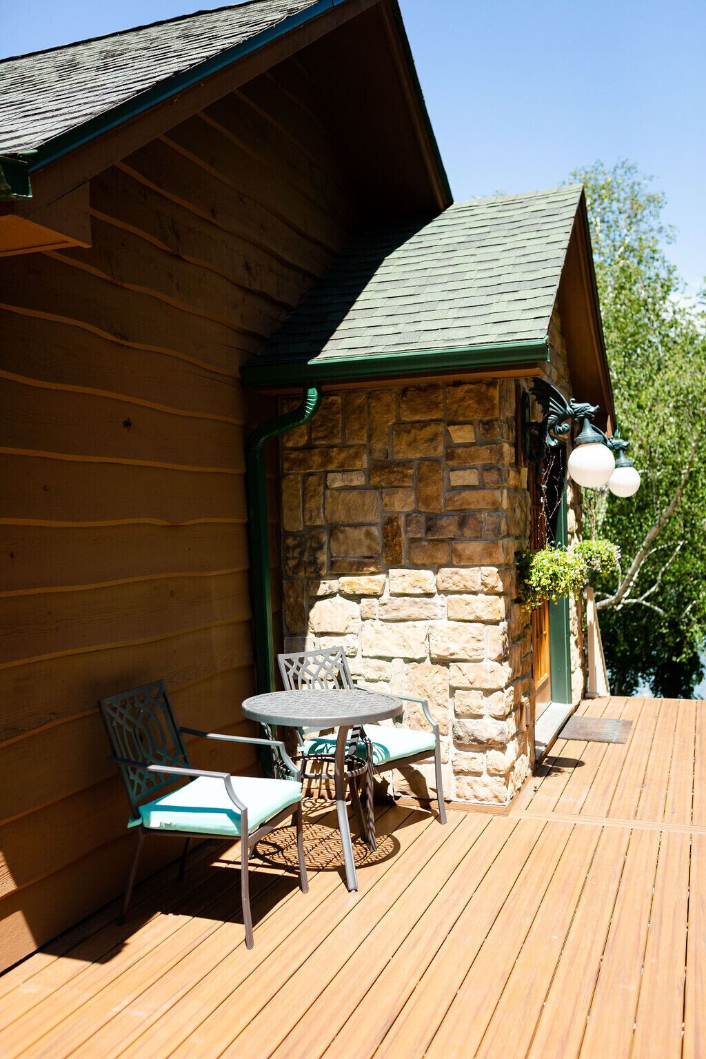 Eine Holzhütte mit einer Steinsäule, einer Terrasse mit Tisch und Stühlen sowie einer hängenden Leuchte.