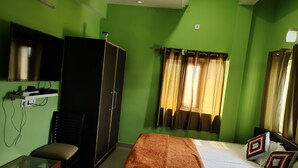 Een kamer met groene wanden, een bed met een bruine deken, een bureau met stoel, een kledingkast en een televisie aan de muur.