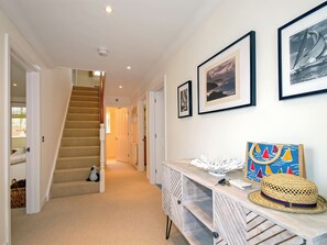 Un couloir avec un escalier, une console sur laquelle est posé un chapeau, et des tableaux encadrés accrochés au mur.