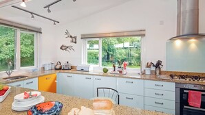 A modern kitchen with granite countertops, a stainless steel range hood, and a large window overlooking a garden.