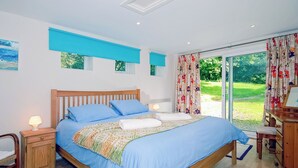 A bedroom with a wooden bed, blue bedding, a nightstand with a lamp, and a view of a garden through a glass door.