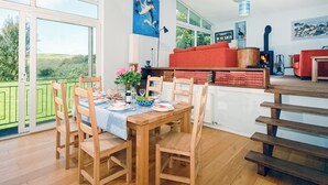A dining area with wooden chairs and a table set for four, a red sofa, a wooden staircase, and a view of the outdoors.
