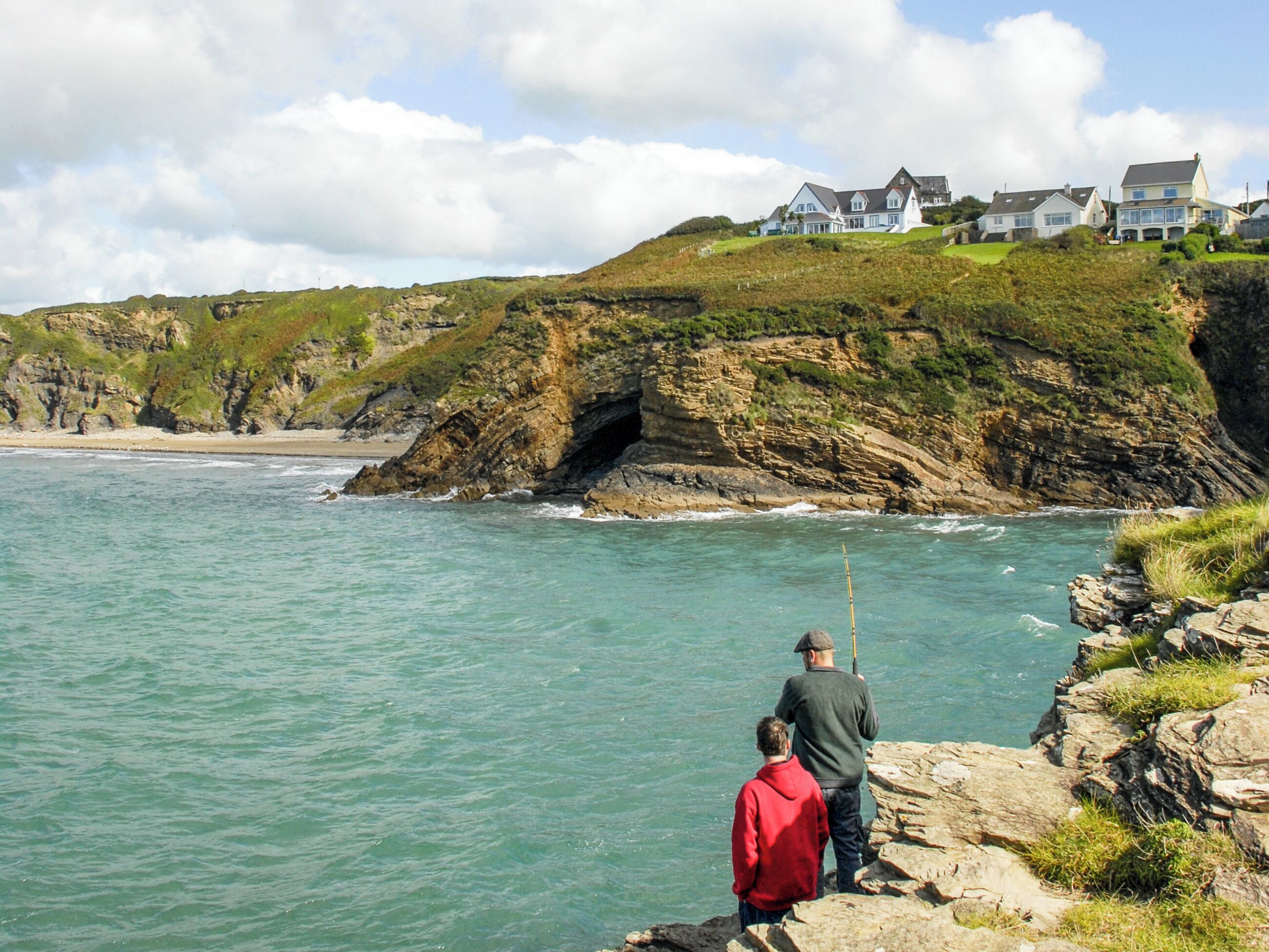 A coastal scene with rocky cliffs, a beach, and houses on a hillside.