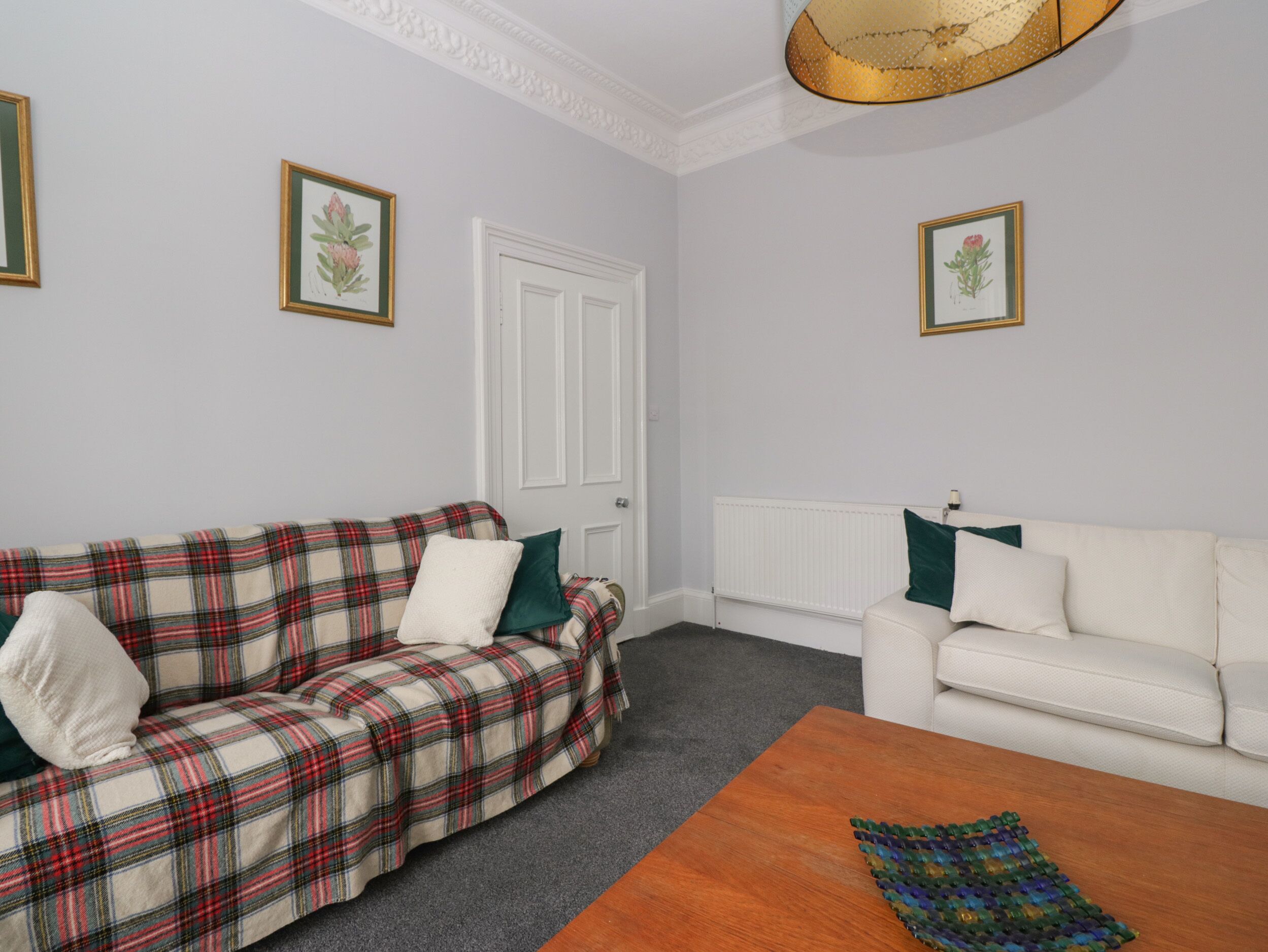 A room with two sofas, one plaid and one white, a wooden coffee table, and a radiator.