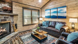 Ein gemütliches Wohnzimmer mit Kamin, Ledersofa und einem großen Gemälde von Bergen.