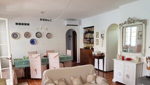 Un soggiorno con divano beige, tavolo da pranzo e sedie. Si nota anche una libreria, uno specchio e un armadio.