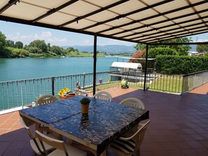 Un portico coperto con tavolo e sedie, con vista su un lago e montagne sullo sfondo.