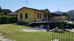 Una villa gialla con un balcone, un vialetto in pietra e uno scooter parcheggiato.