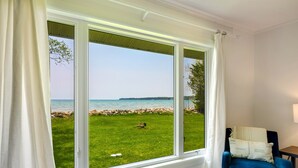Ein Zimmer mit großem Fenster und Blick auf eine Wiese sowie ein Gewässer.