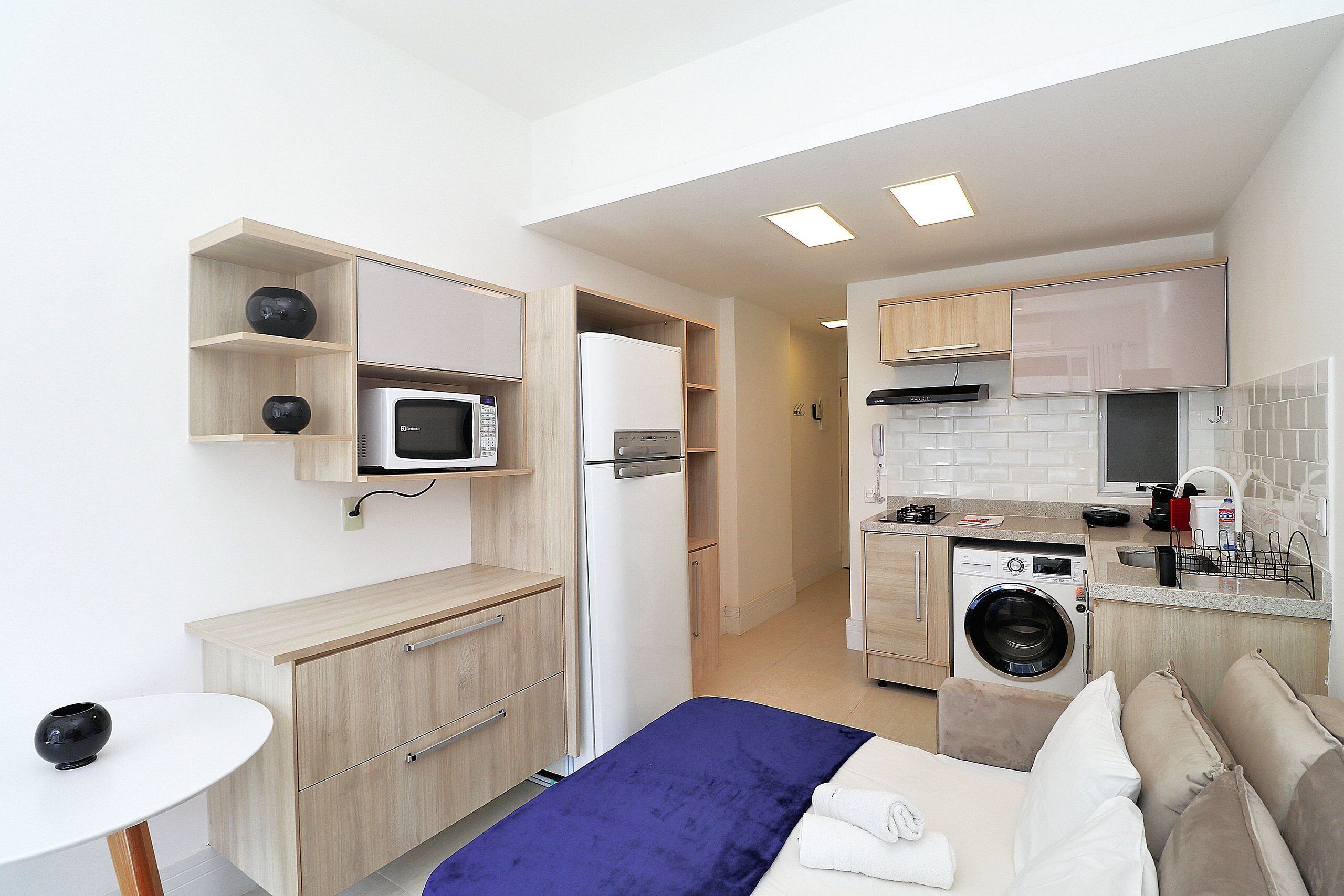 Habitación de hotel pequeña con cama, un escritorio, microondas, refrigerador, lavadora y kitchenette.