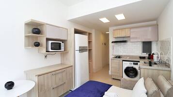 Habitación de hotel pequeña con cama, un escritorio, microondas, refrigerador, lavadora y kitchenette.