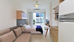 A compact hotel room with a bed, a sofa, a desk with a chair, a microwave, and a television. - Rio Spot Homes C056 (Rio de Janeiro)