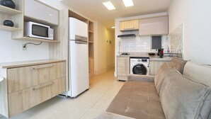 A compact kitchen with a microwave, refrigerator, washing machine, and a beige sofa in a modern apartment. - Rio Spot Homes C056 (Rio de Janeiro)