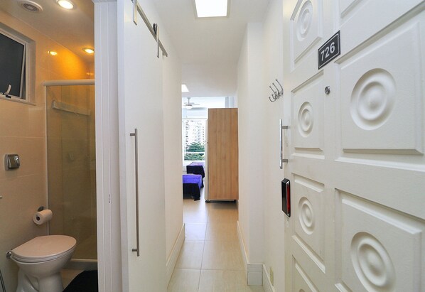 A hotel hallway with a toilet, shower, and a door with a number sign.