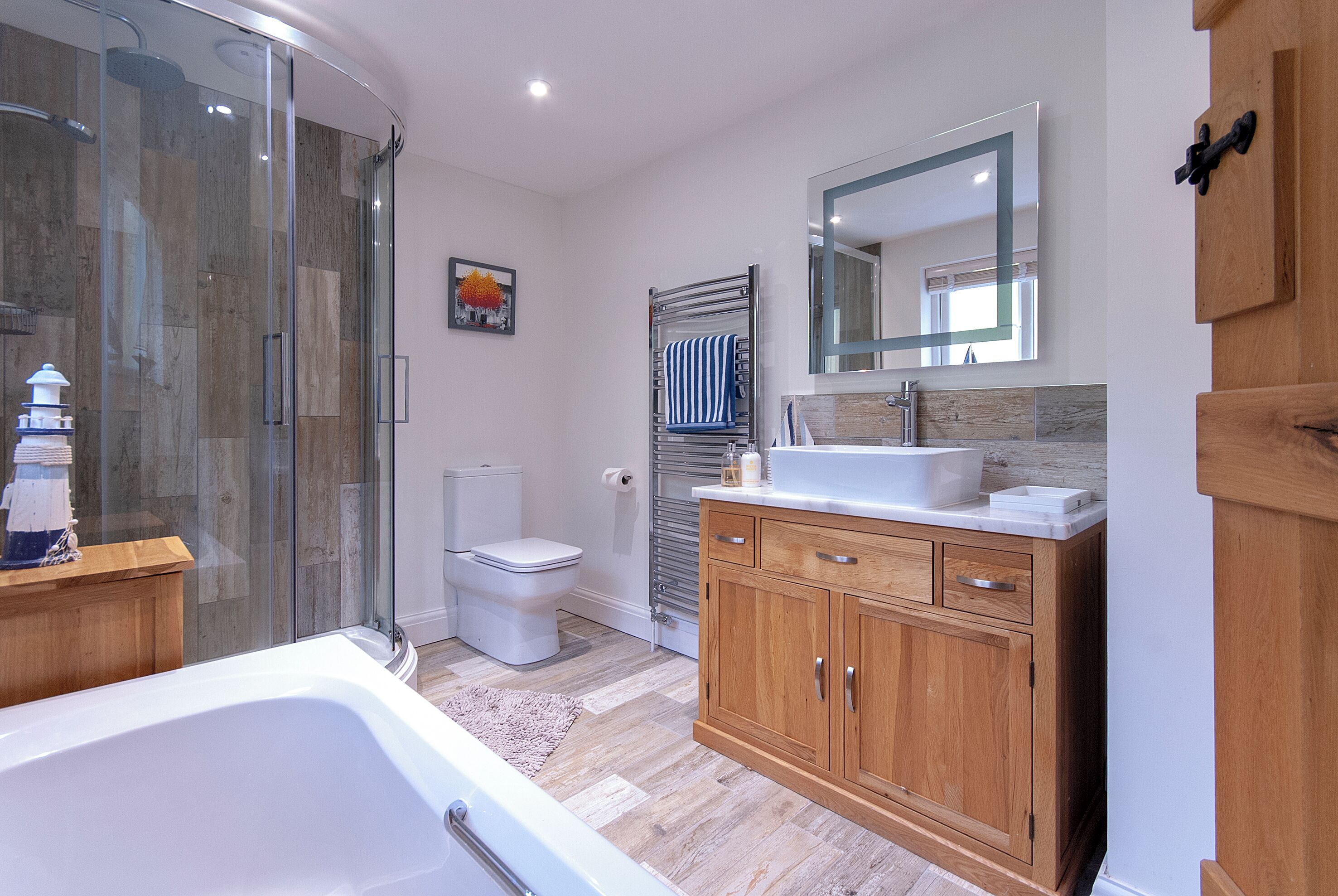 A modern bathroom with a glass shower enclosure, a white bathtub, a wooden vanity with a mirror, and a toilet.