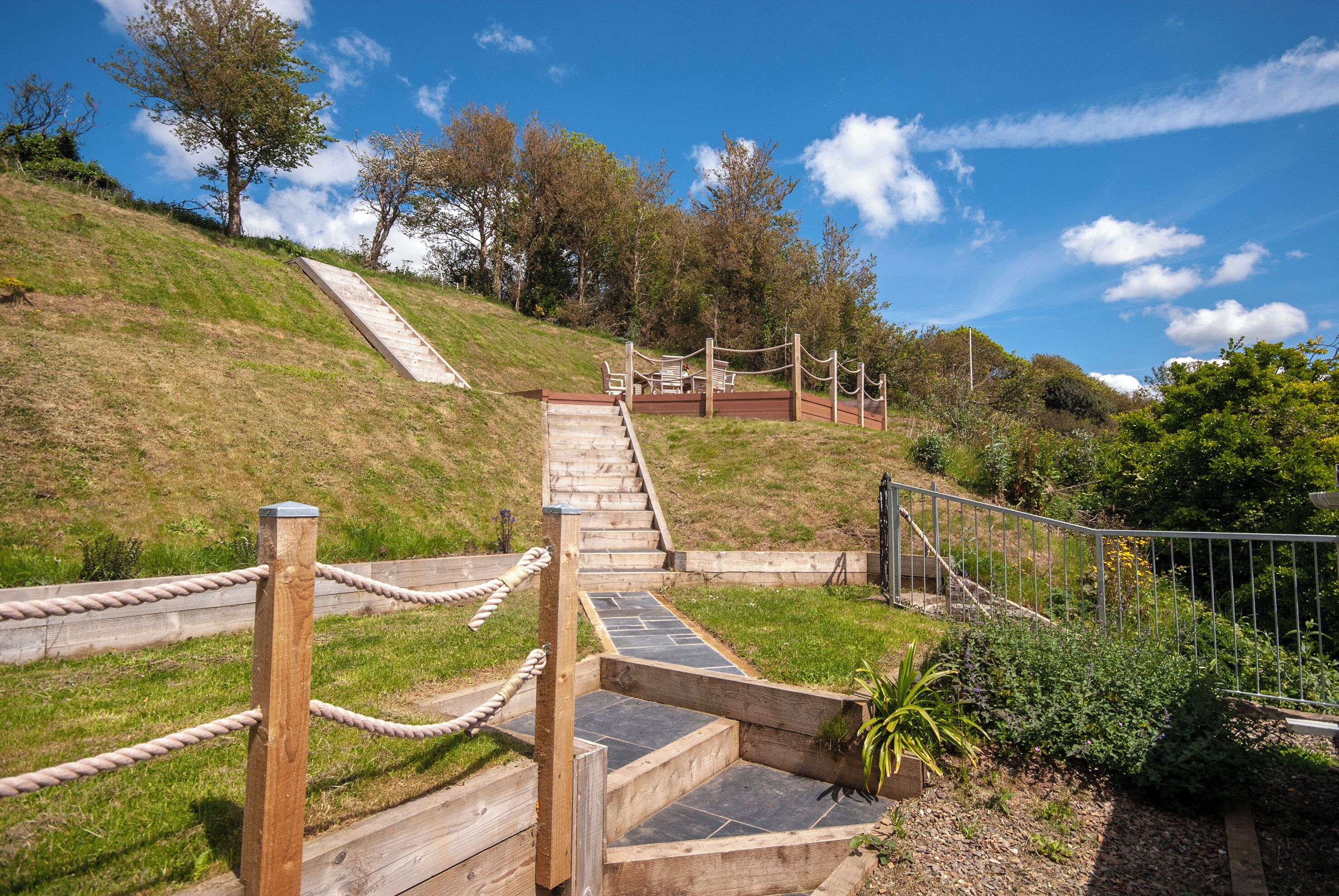 A wooden staircase leading up a grassy hill with a metal fence and rope barrier.