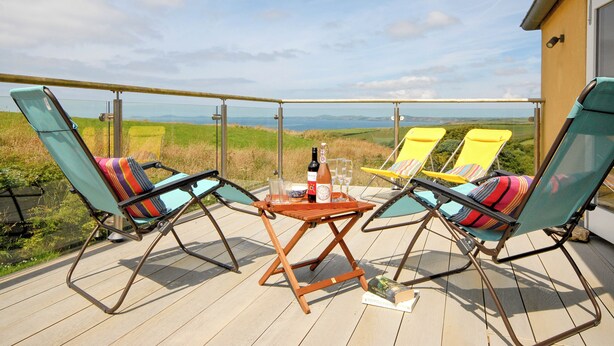 A balcony with two lounge chairs, a table with a bottle and glasses, and a view of the countryside. - Druidston Old Farmhouse (Druidston Haven)