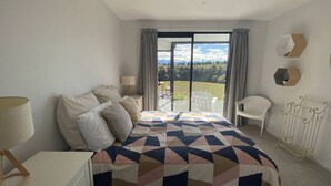 A bedroom with a bed, a nightstand, a chair, and a view of the outdoors.