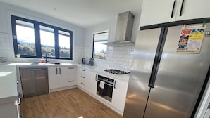 A modern kitchen with white cabinets, a stainless steel refrigerator, a built-in oven, and a window with a view of trees.